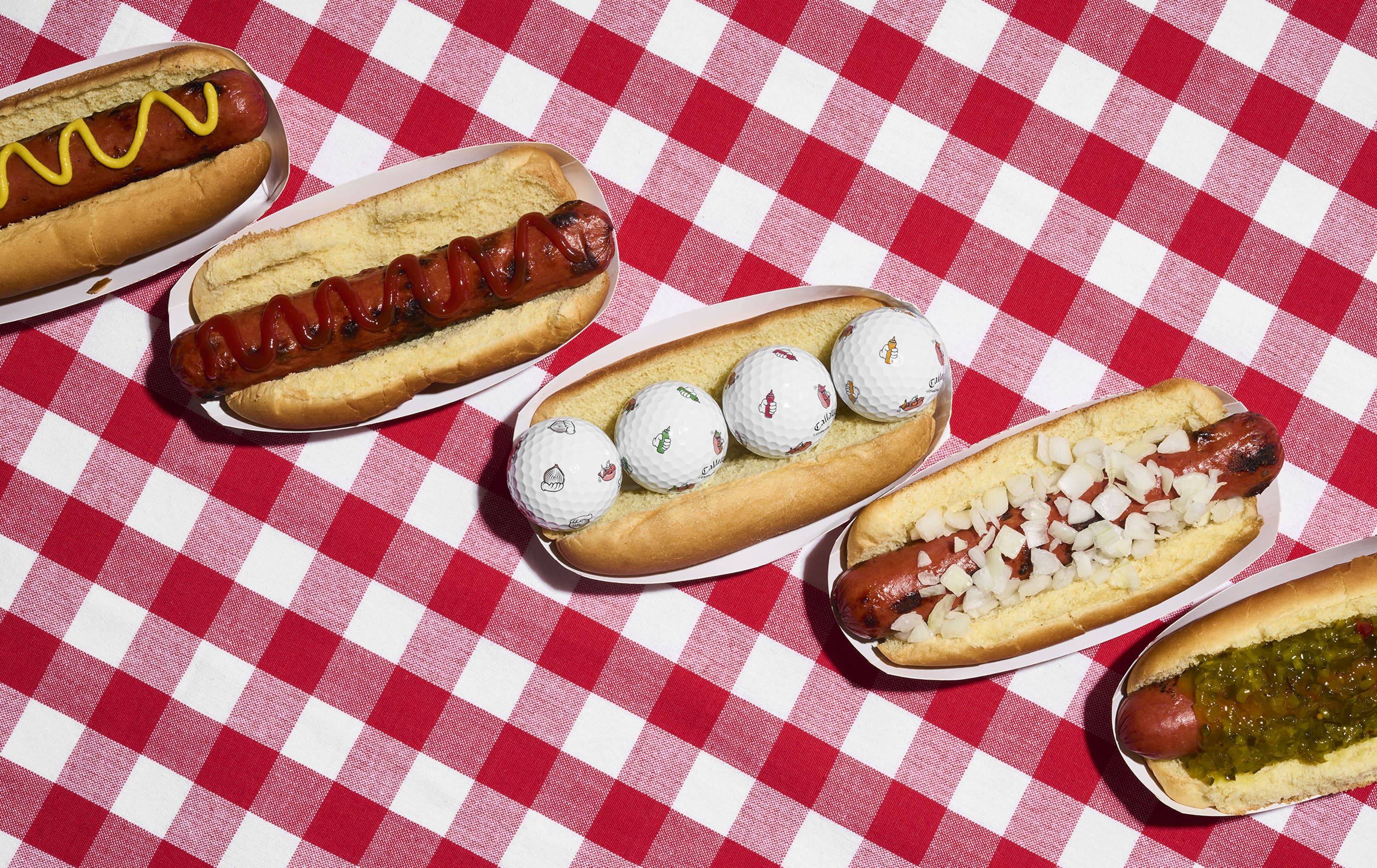 chrome tour golf balls with hot dog designs in a hot dog bun on a picnic table