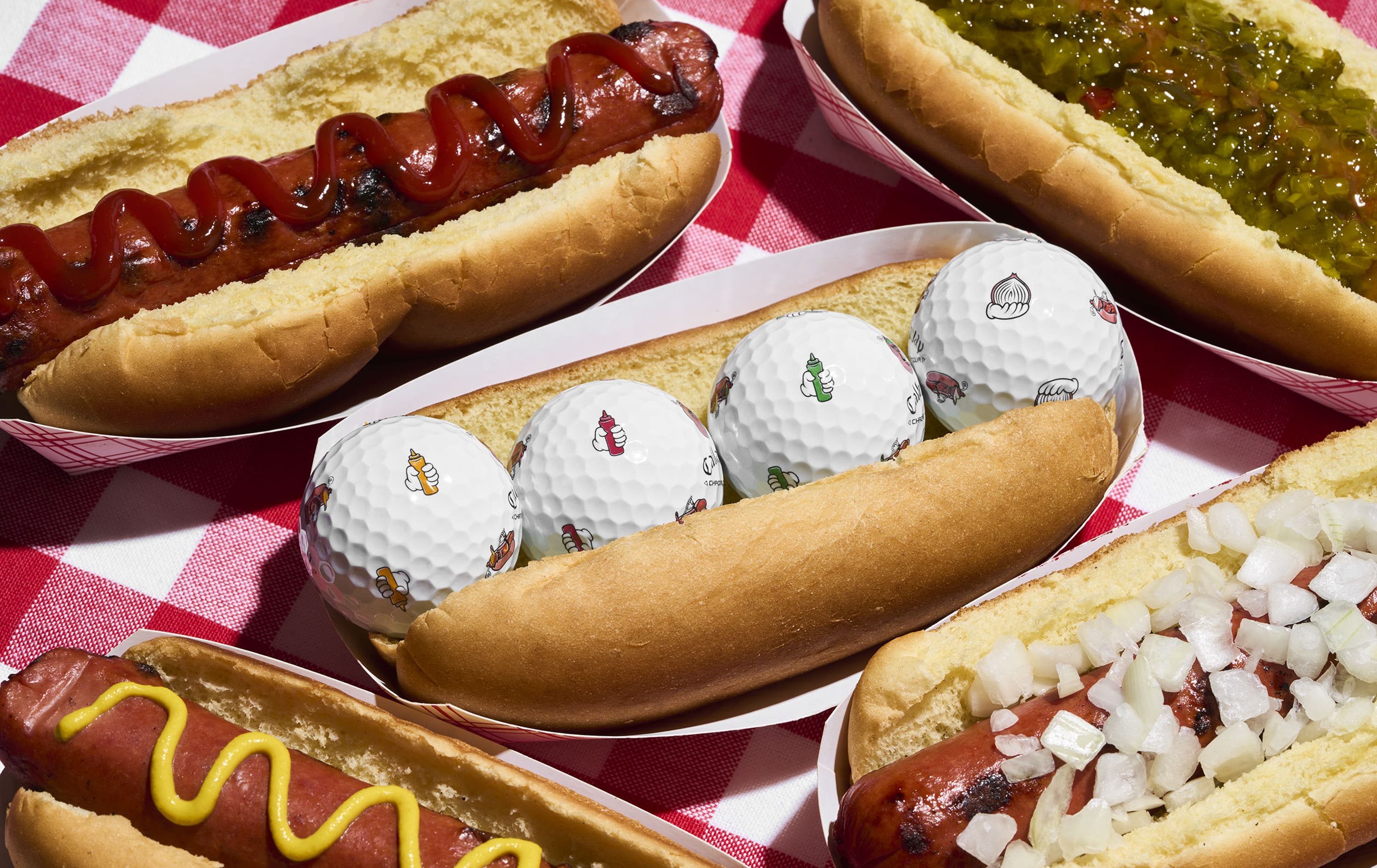 chrome tour golf balls with hot dog designs in a hot dog bun on a picnic table