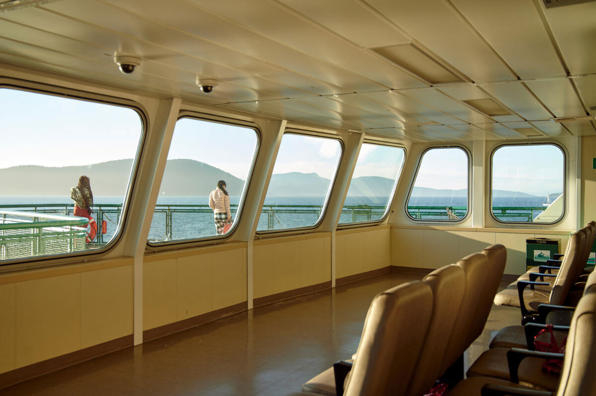 From inside of a ferry, a view to two women standing on the deck and the water beyond.