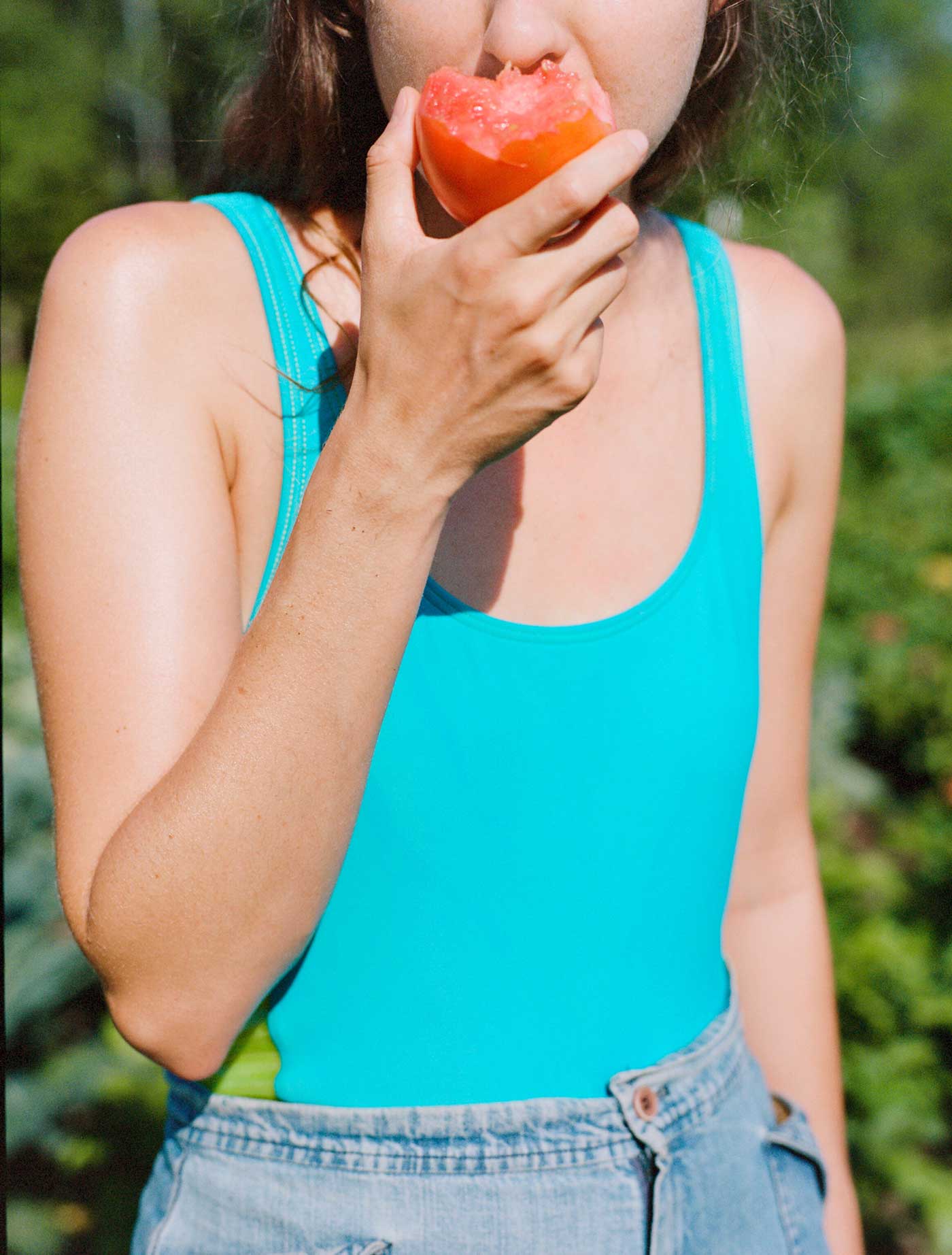A person in a swimsuit and shorts eats a piece of fruit.