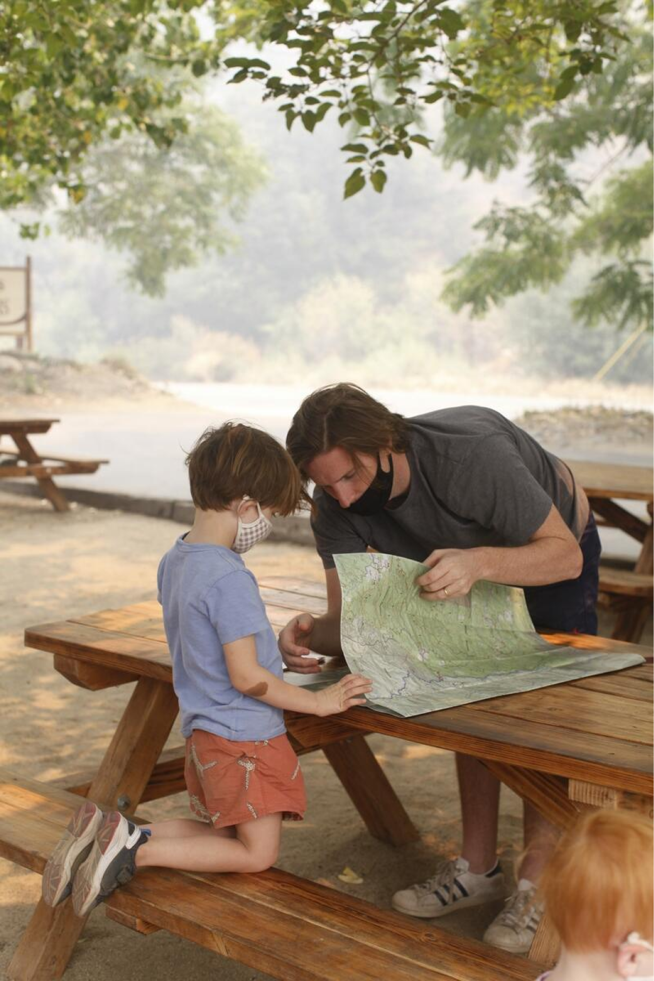 A man and boy wear medical masks as they look at a roadmap atop a picnic table.