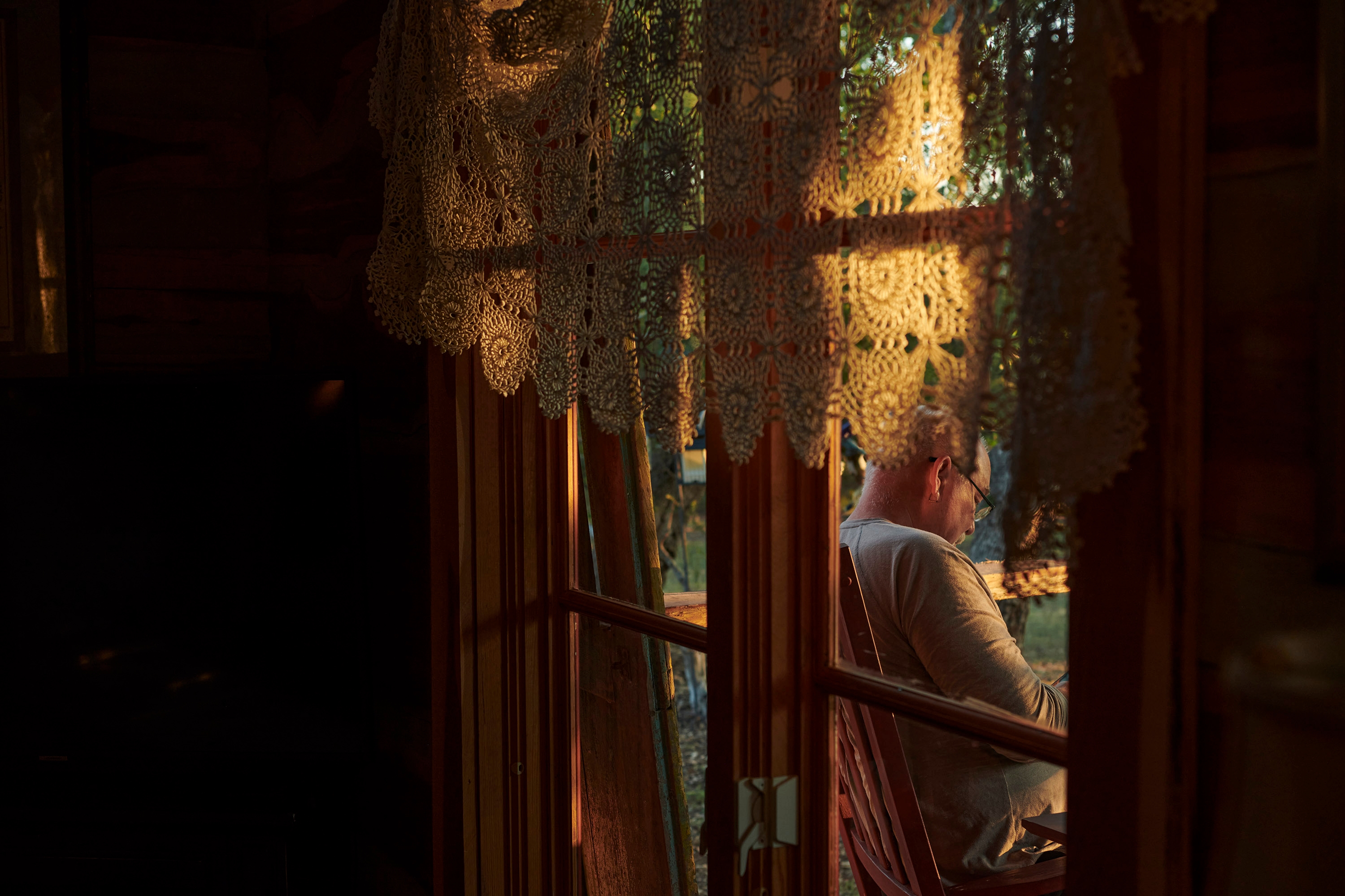 Sunrise through a window of a cabin which shows the photographer's father Steve sitting on the porch.
