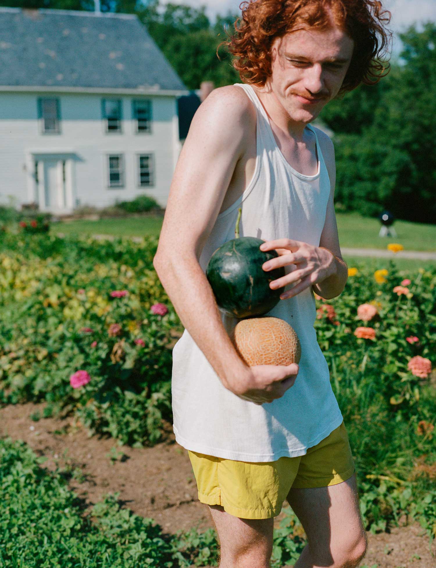A person walks through a garden holding two melons.
