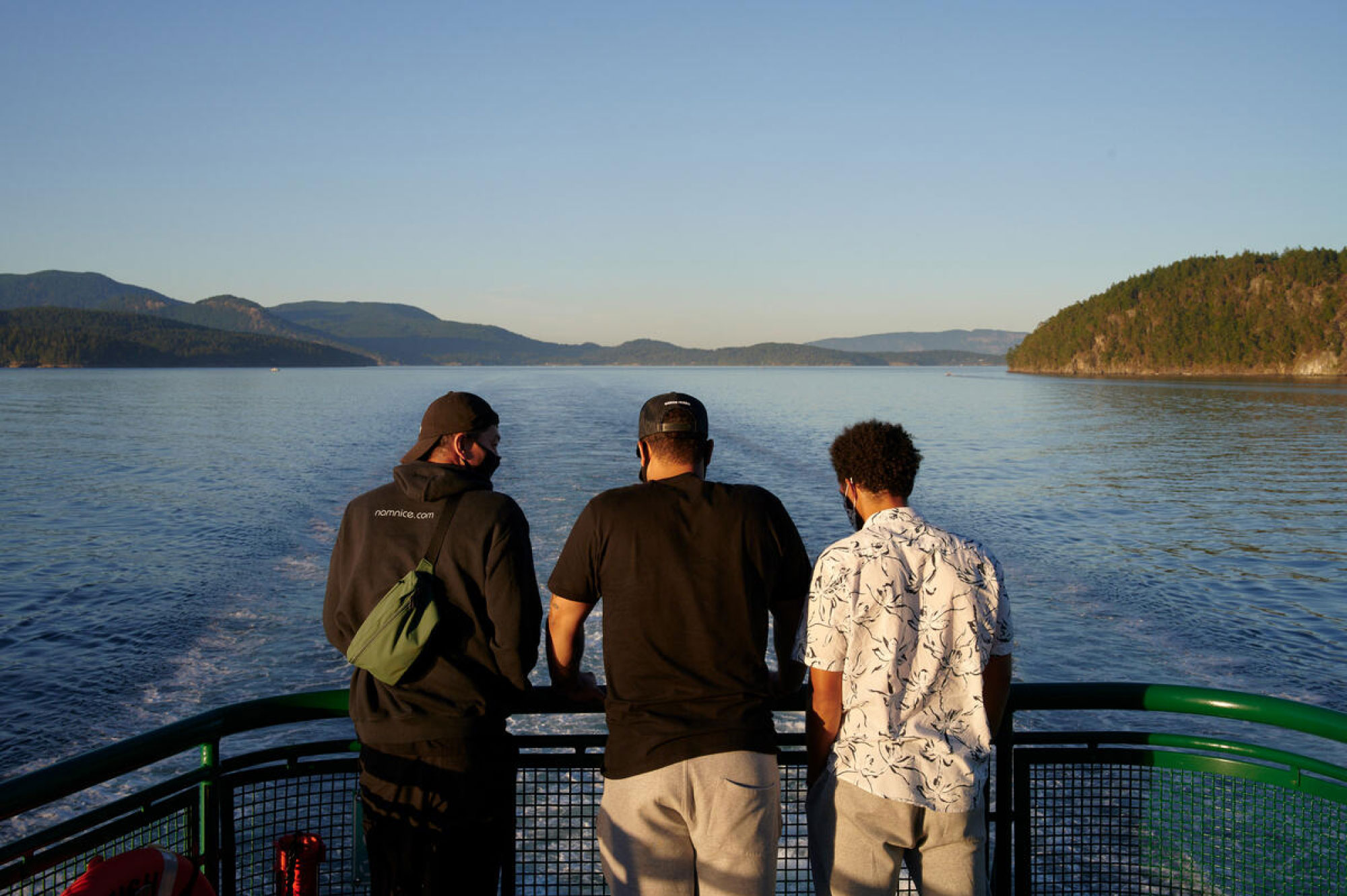 Three men stand at the front of a ferry boat, looking out onto the water.