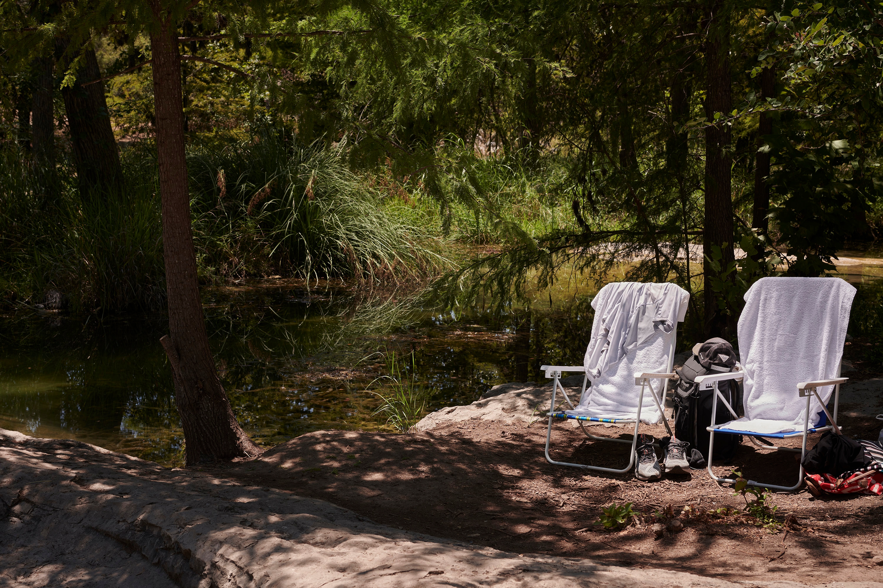 Two folding chairs with towels draped over them on the bank of Krause Springs in Spicewood, Texas.