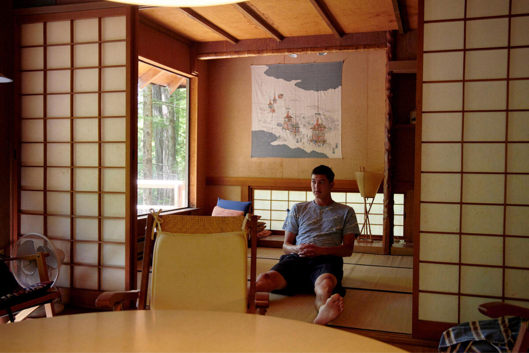 A man sits on a tatami mat floor inside of a japanese-inspired room.