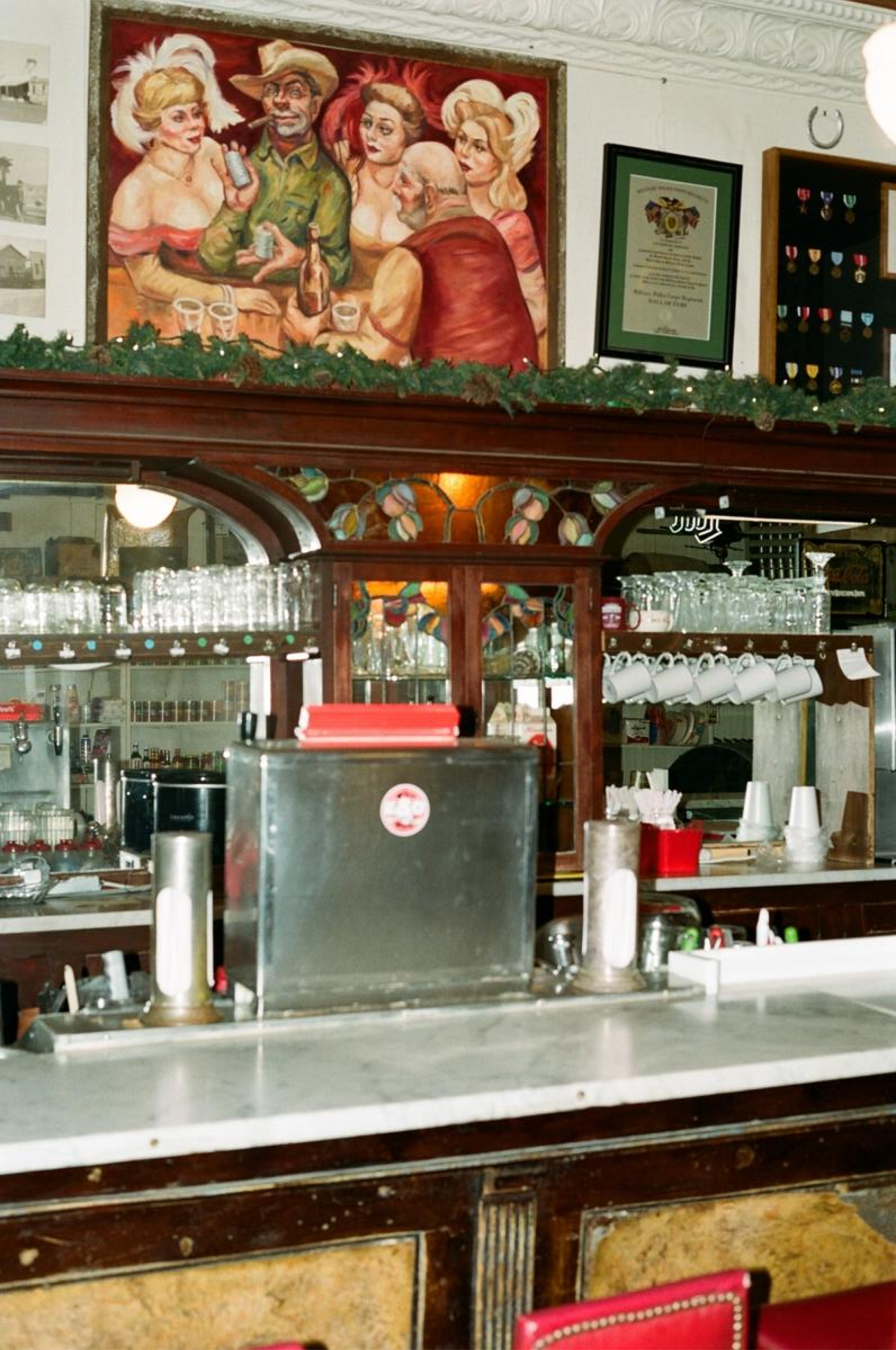 A marble counter top bar, with a soda dispenser on top and mugs hanging above.