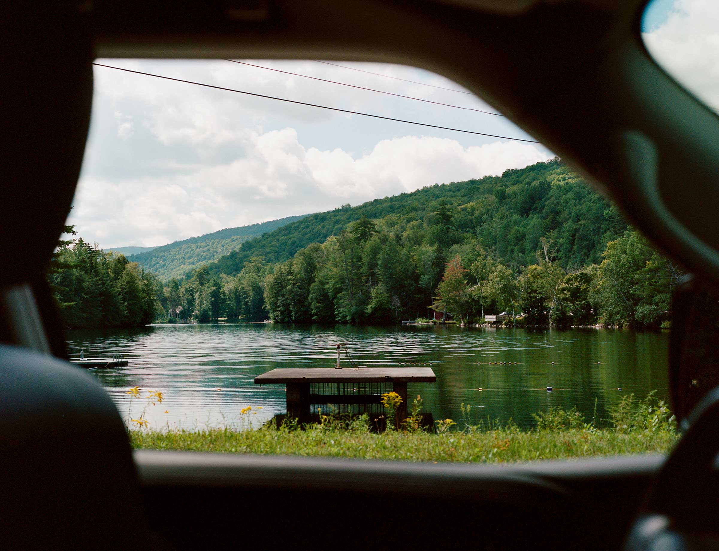 Through a car window: a lake surrounded by trees and hills.