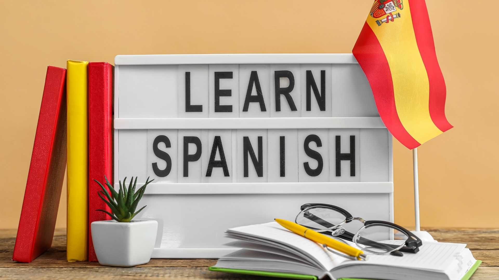 Tablica z napisem Learn Spanish, zeszyt, długopis i hiszpańska flaga