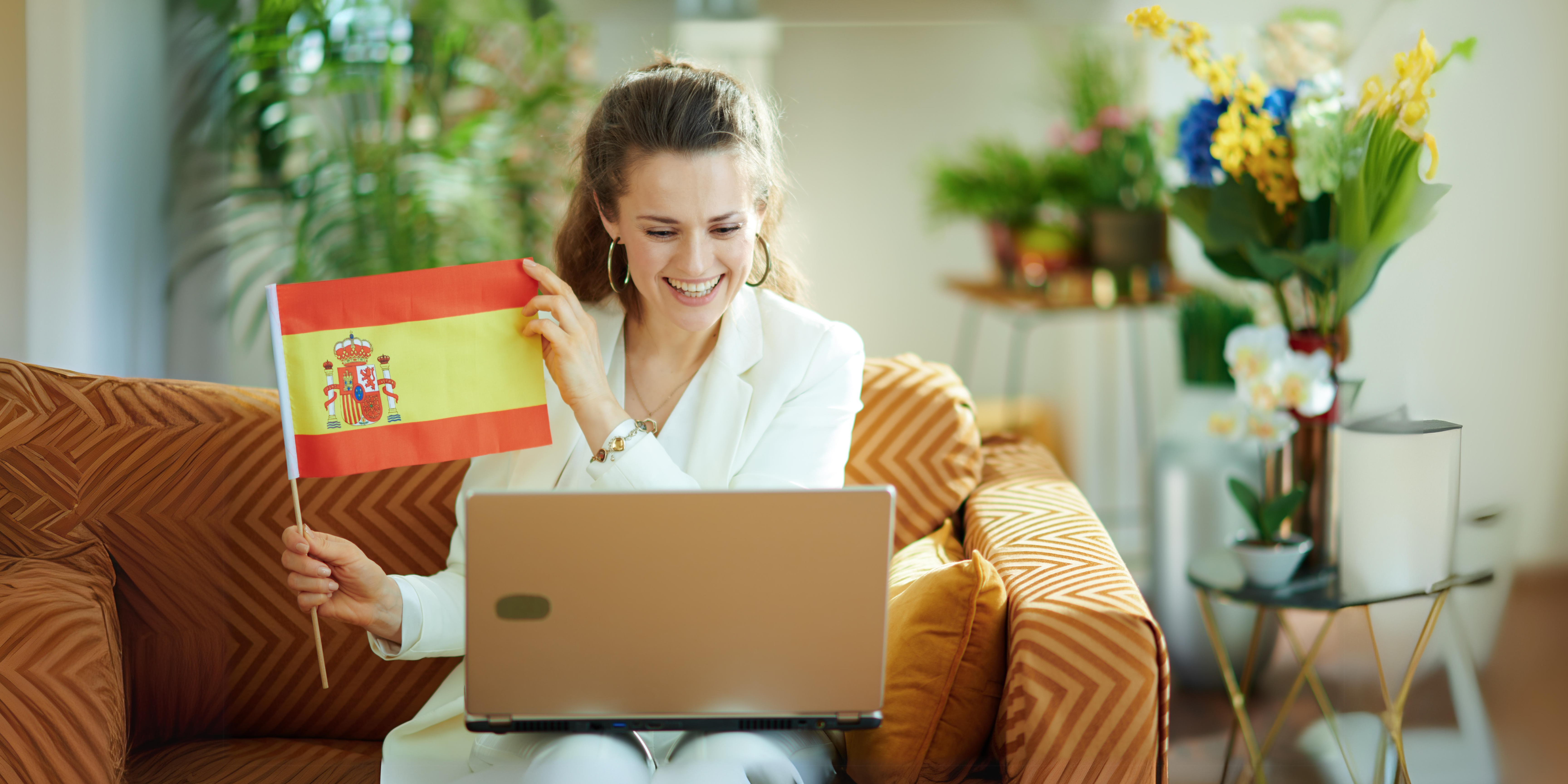 Uśmiechnięta kobieta uczy się hiszpańskiego online z laptopa