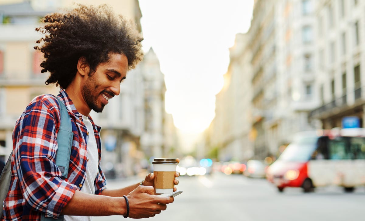 Młody mężczyzna uczy się języka niemieckiego na telefonie po zakupie kawy