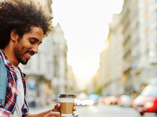 Młody mężczyzna uczy się języka niemieckiego na telefonie po zakupie kawy