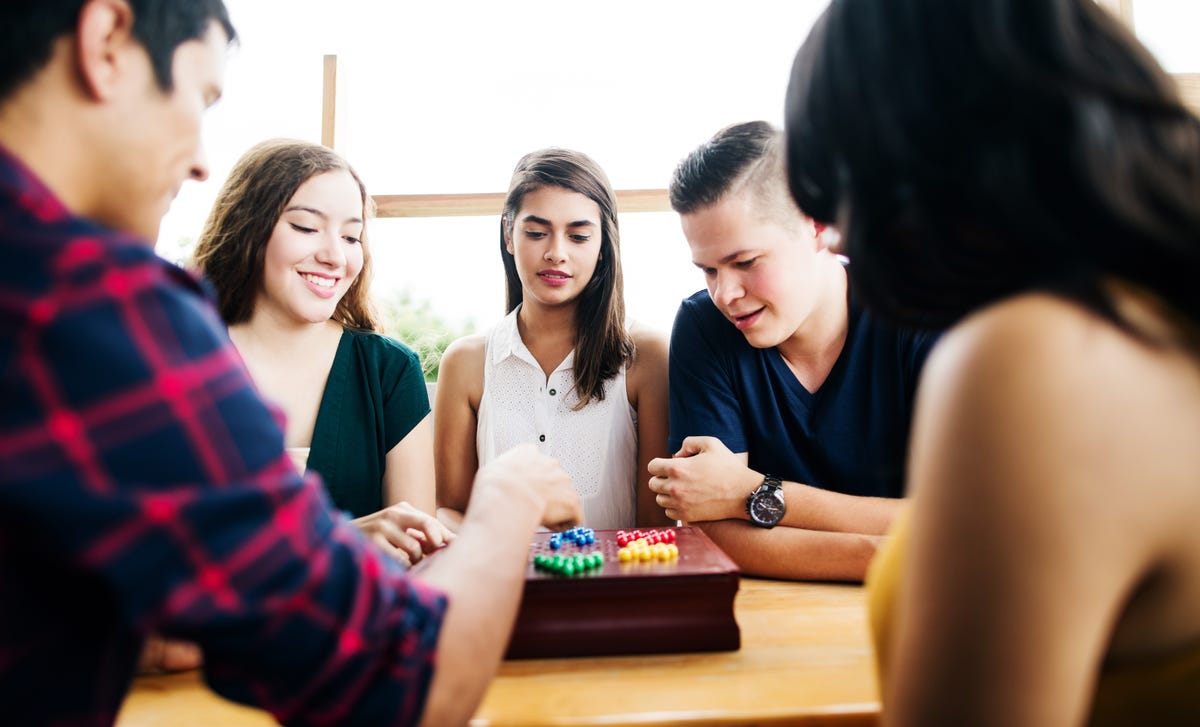 Grupa nastolatków grających w planszówki podczas kursu językowego, aby ćwiczyć niemiecki w codziennych sytuacjach.