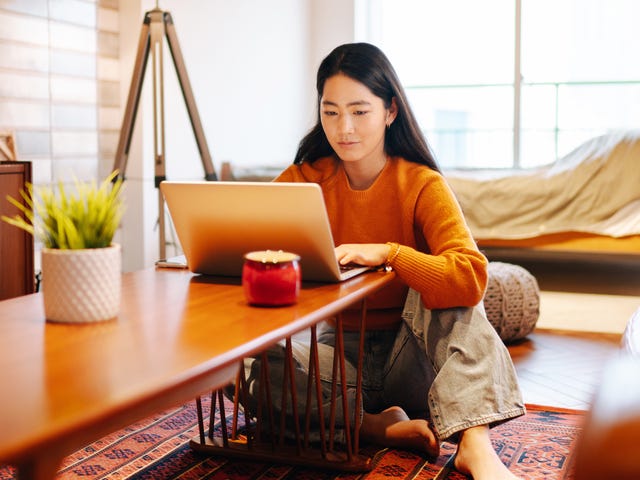 Kobieta siedząca na podłodze z laptopem na stoliku kawowym na kursie angielskiego dla początkujących