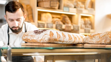 Pracownik piekarni wykłada croissanty na sprzedaż.