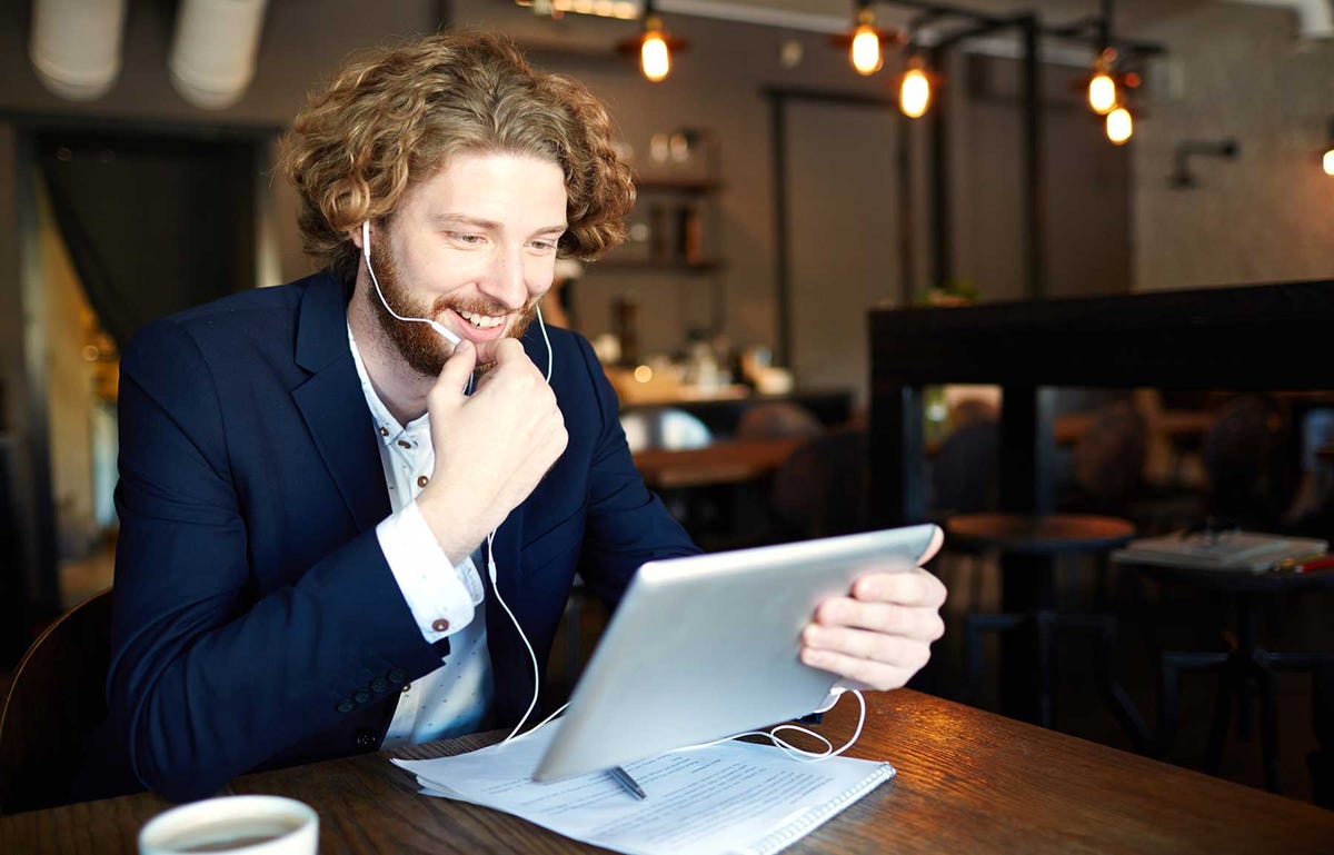 Mężczyzna siedzący w kawiarni ze słuchawkami i uczący się hiszpańskiego online na tablecie