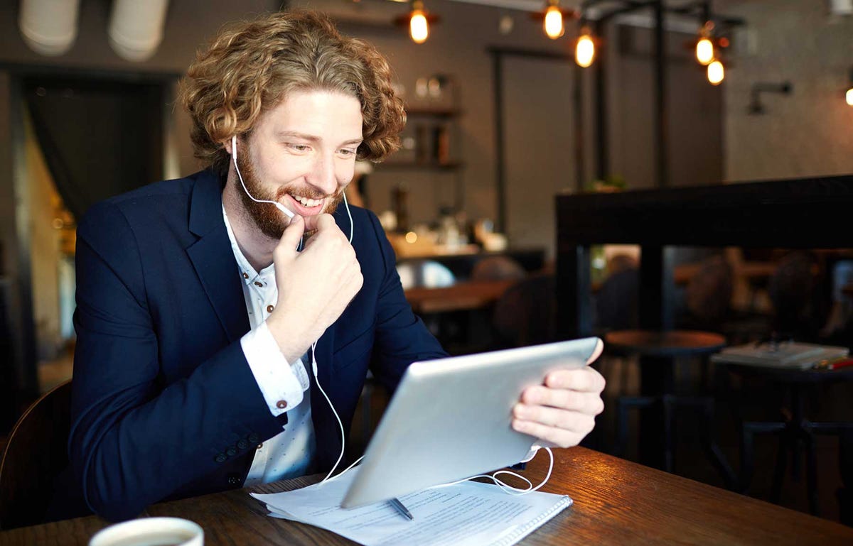 Mężczyzna siedzący w kawiarni ze słuchawkami i uczący się hiszpańskiego online na tablecie