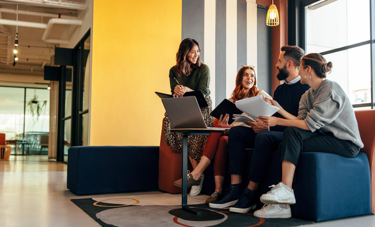 Pracownicy rozmawiający i śmiejący się razem, siedzący na kanapie w firmie.