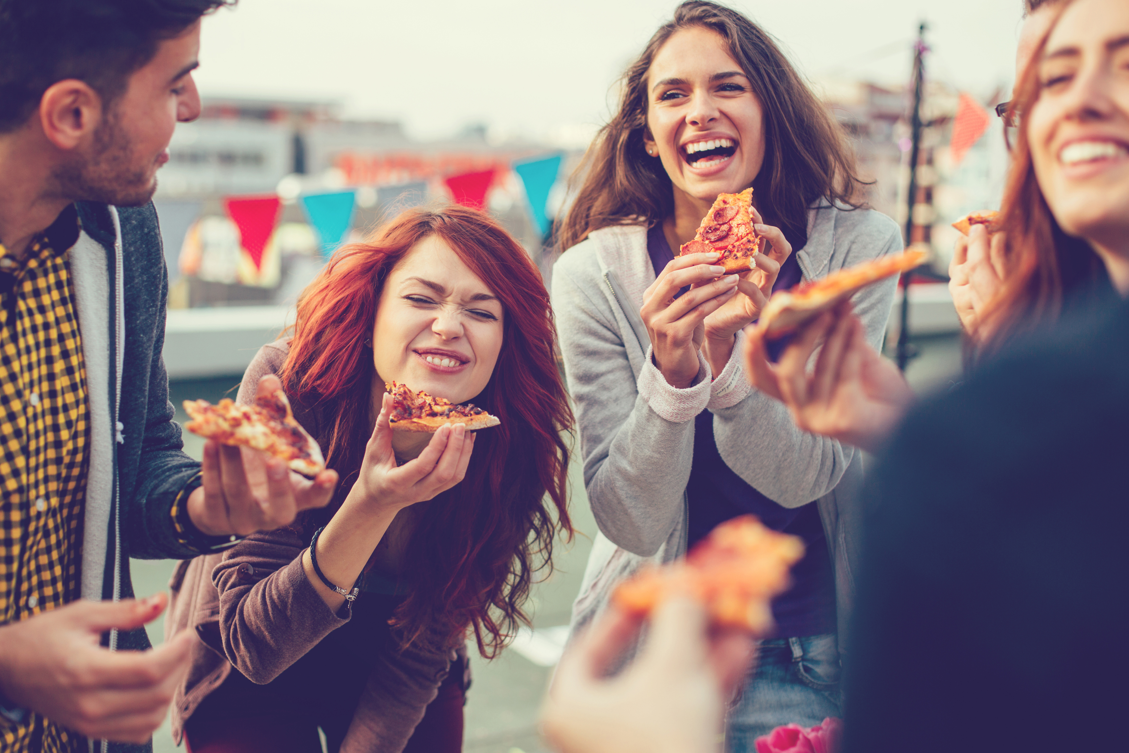 Grupa młodych dorosłych wspólnie spędza czas, je pizze i śmieje się. 