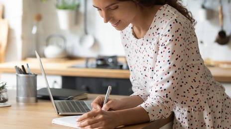 Kobieta robi notatki podczas zajęć z hiszpańskiego online z domu.