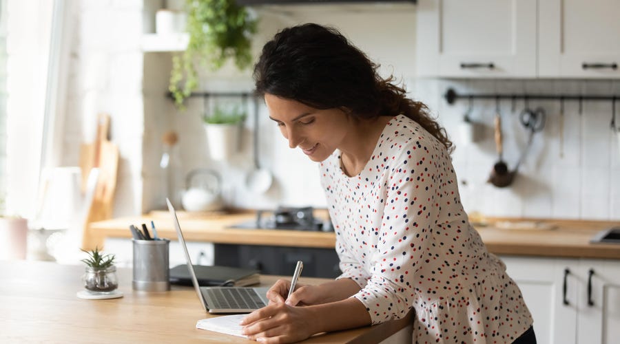 Kobieta robi notatki podczas zajęć z hiszpańskiego online z domu.