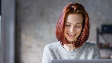 Kobieta uśmiechająca się do laptopa podczas lekcji angielskiego przez internet