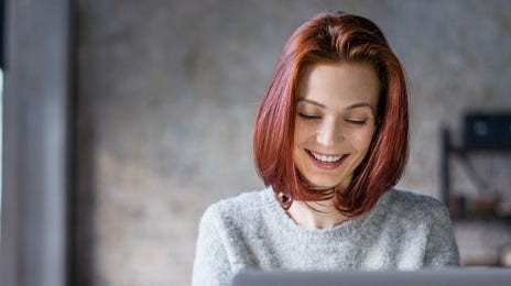Kobieta uśmiechająca się do laptopa podczas lekcji angielskiego online.