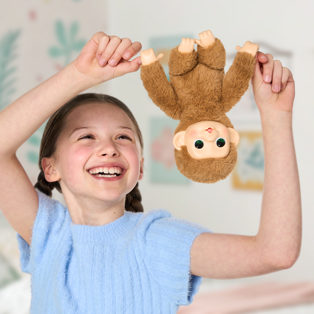 Girl smiling while holding her mini monkey toy upside down beside her head. 