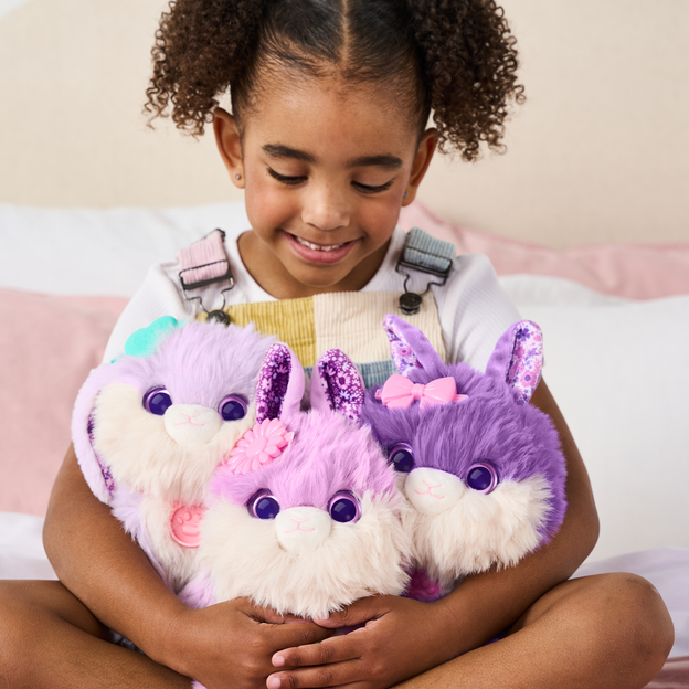 Young girl holding 3 purple ScruffaLuvs toys in her arms. 
