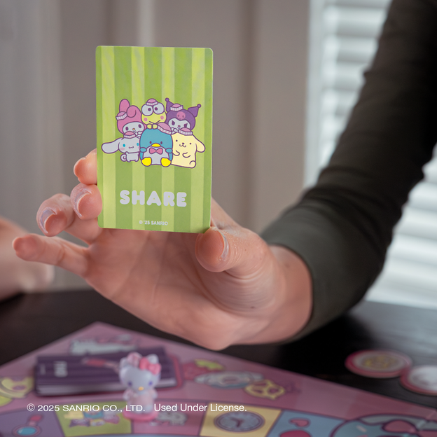 Woman holding up a green activity card from the Hello Kitty and Friends Snack Shop game.