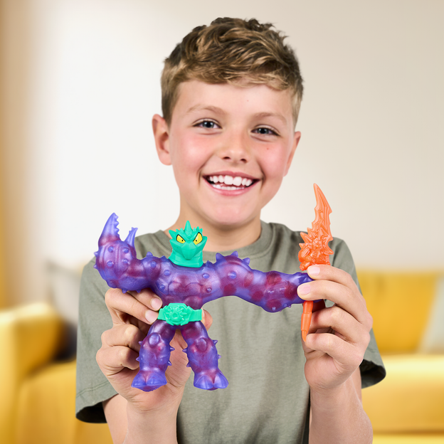 Young boy smiling while holding a purple Heroes of Goo Jit Zu action figure with red sphere.
