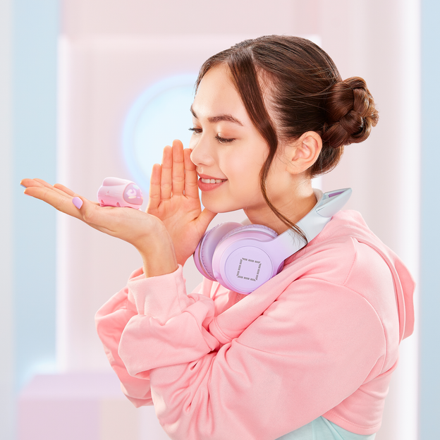 Young girl facing the left smiling at pink micropet toy, she is holding one hand up to her mouth as if she is whispering at the toy.