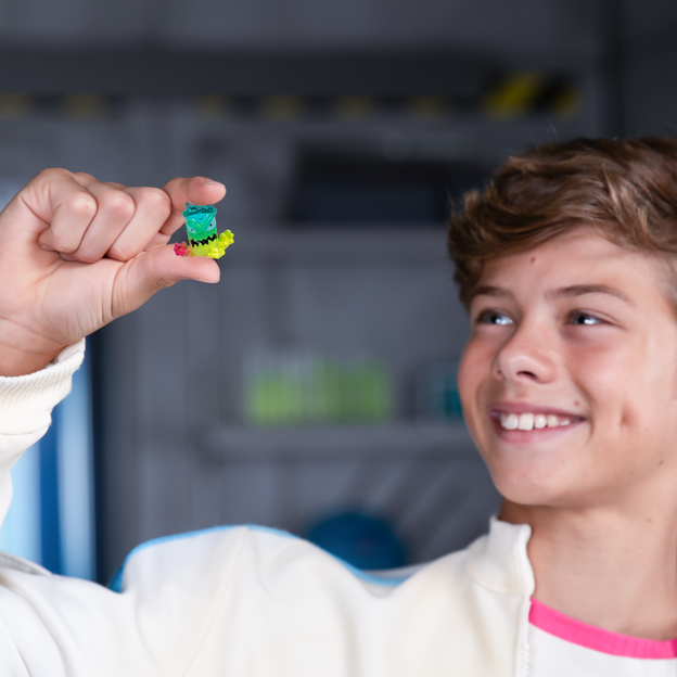 Young boy in white jacket holding a mini Mrbeast Lab Swarms character up in his right hand.