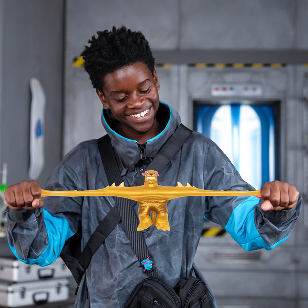 Young boy in an oversized jacket stretching a gold MrBeast Lab stretchy hero toy by its arms.