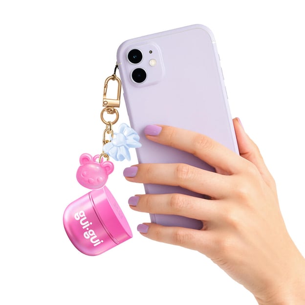 Hand holding phone in purple case with pink mini Gui Gui keychain hanging off it. 