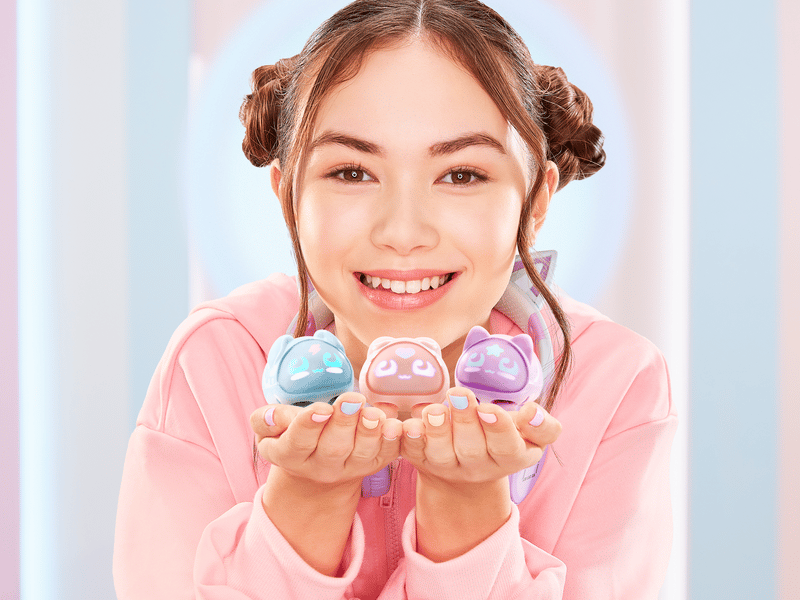 Young girl smiling at the camera holding up three different micropet toys, all different colors, under her chin.
