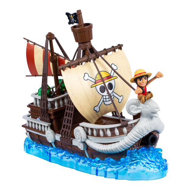 One Piece Going Merry Deluxe Collector Ship. The ship is brown and displayed on water. There is a mini action figure sitting at the front of the ship. The ship has cream colored sails with a skull and crossbones wearing a straw hat.