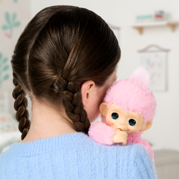 Girl with brown braided hair hugging a pink mini monkey toy over shoulder.