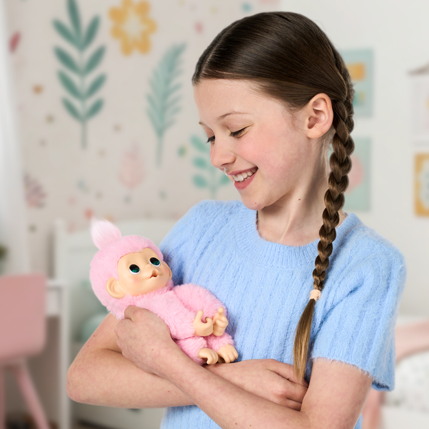 Girl in a light blue shirt cradling her pink mini monkey toy.