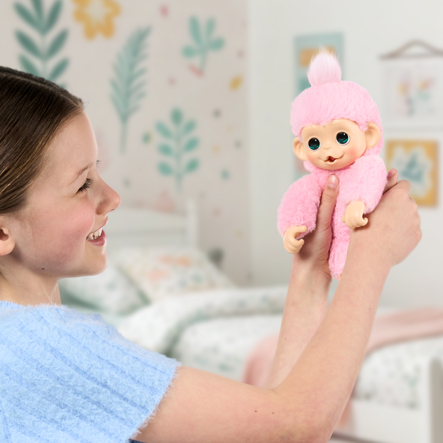 Girl in a light blue shirt holding up her pink mini monkey toy in the air.
