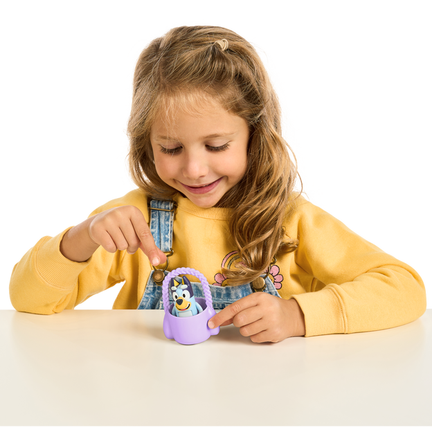 Young brunette girl placing a small bluey figure inside a purple easter egg basket.
