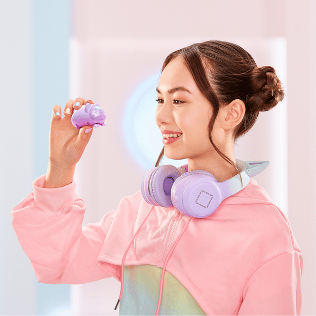 Young girl smiling and facing the left, she is holding up a purple micropet toy. She is wearing pastel colors to match the color of the toy.