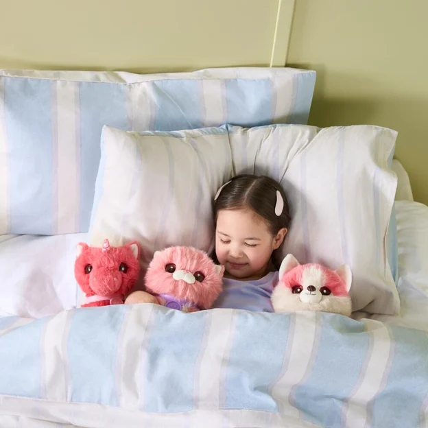 Little girl tucked in bed with three ScruffaLuvs S3 Pet Single Pack Coral Pet toys.