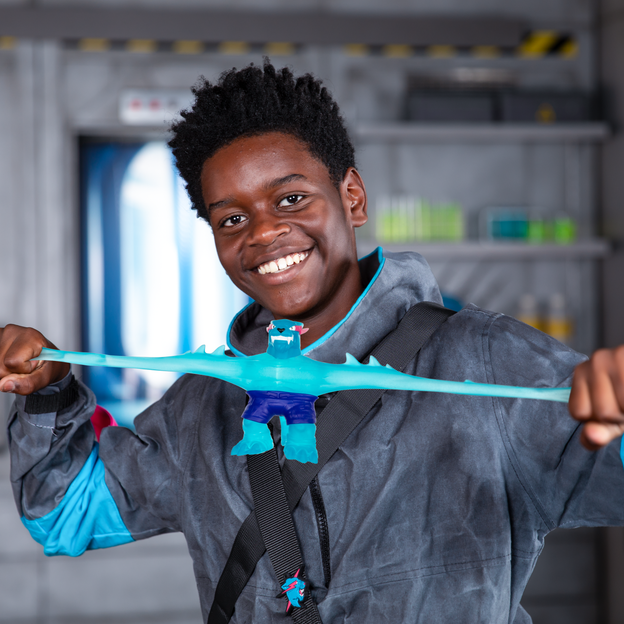 Young boy in an oversized jacket stretching a light blue MrBeast Lab stretchy hero toy and smiling.