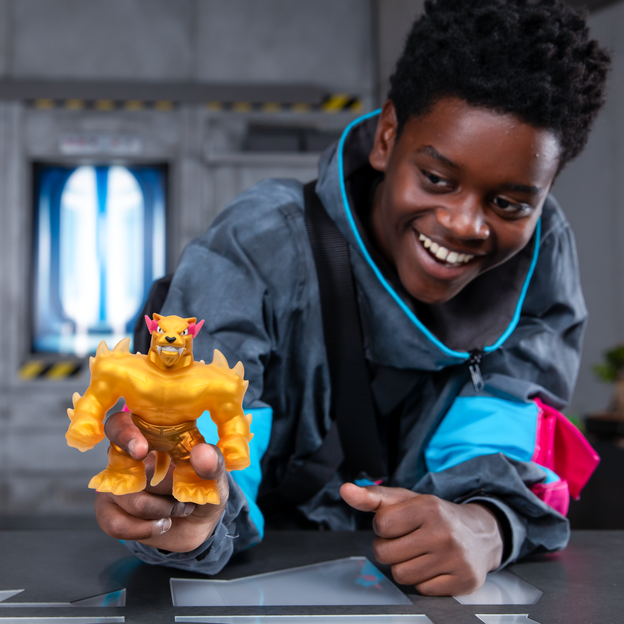 Young boy in an oversized jacket holding out a gold MrBeast Lab stretchy hero toy.