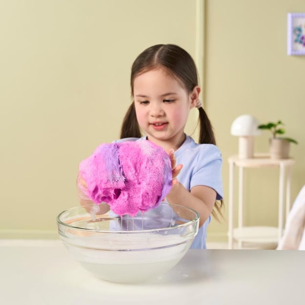 Young girl washing a pink ScruffaLuvs Tiedye toy in a bowl of water. 