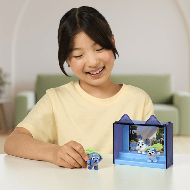 Young girl sitting down, playing with 3 fuzzy Bluey characters in their display case.