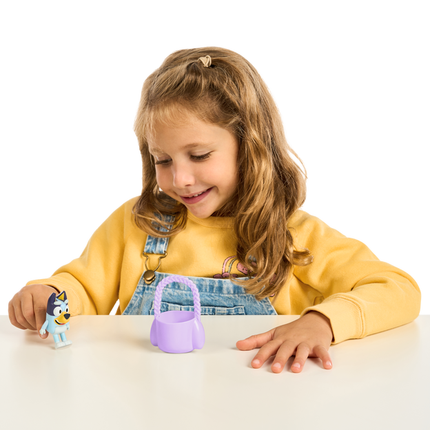 Young brunette girl playing with small bluey figure and purple easter egg basket.