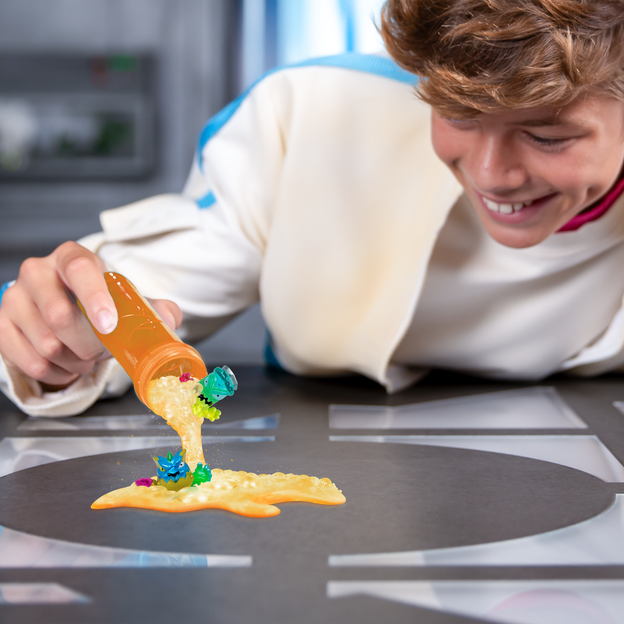 Young boy in white jacket pouring out swarms from orange test tube.