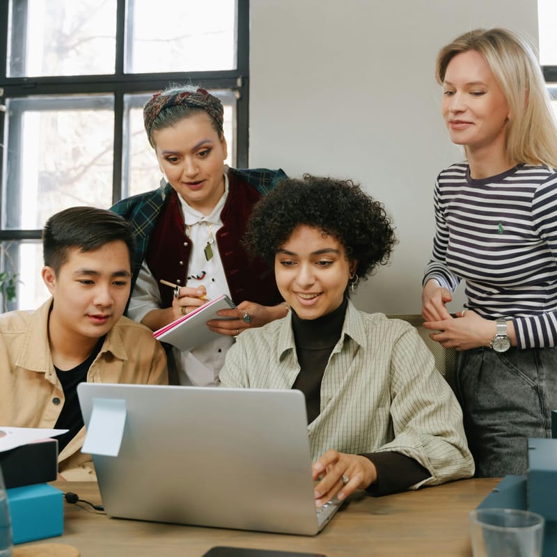 Grupo de adultos reunidos frente a una computadora portátil, estudiando sobre el proceso de aprendizaje.